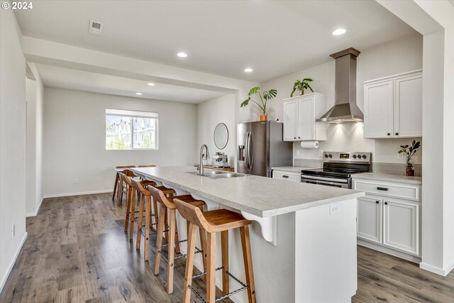 kitchen featuring a center island with sink, wall chimney range hood, white cabinets, appliances with stainless steel finishes, and sink