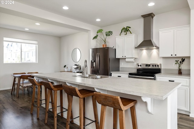 kitchen with a center island with sink, wall chimney exhaust hood, appliances with stainless steel finishes, light countertops, and white cabinetry