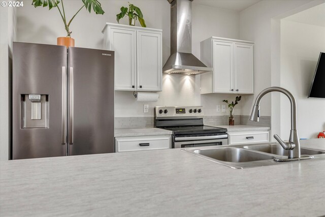 kitchen with sink, stainless steel appliances, wall chimney range hood, and white cabinetry