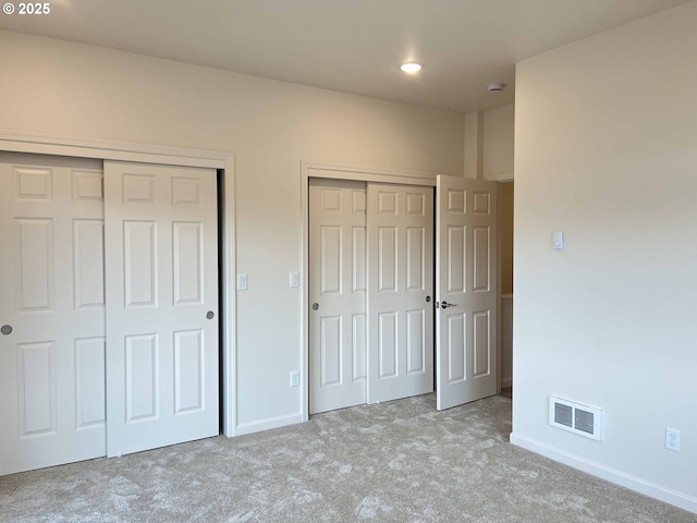 unfurnished bedroom featuring baseboards, visible vents, multiple closets, and carpet flooring