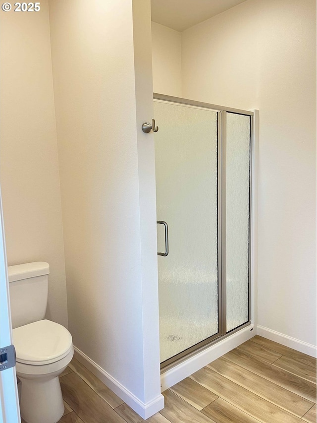 bathroom featuring baseboards, a shower stall, toilet, and wood finished floors