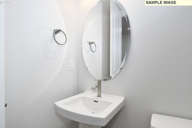 bathroom featuring toilet, a textured wall, and a sink