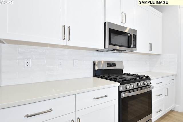 kitchen with white cabinets, backsplash, stainless steel appliances, and light hardwood / wood-style floors