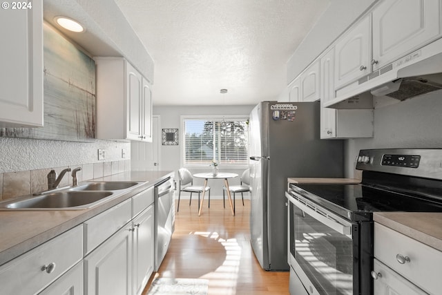 kitchen featuring appliances with stainless steel finishes, sink, white cabinets, hanging light fixtures, and light hardwood / wood-style floors