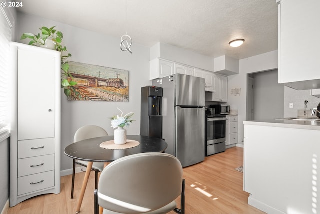 kitchen featuring appliances with stainless steel finishes, light hardwood / wood-style flooring, a textured ceiling, white cabinets, and decorative backsplash