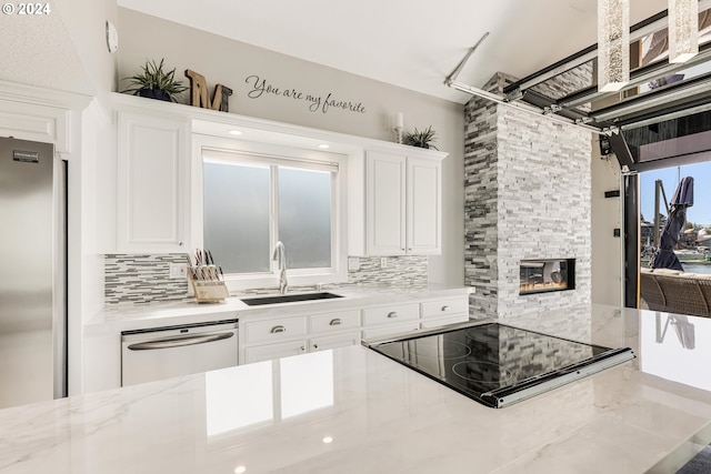 kitchen featuring sink, a stone fireplace, decorative backsplash, white cabinets, and appliances with stainless steel finishes