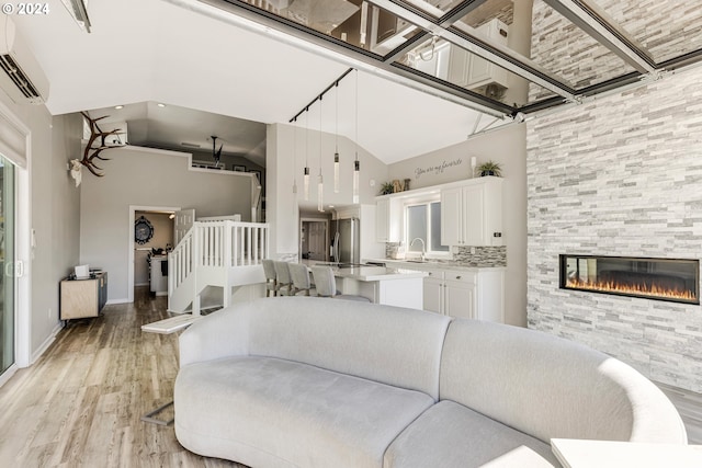 living room featuring light wood-type flooring, sink, high vaulted ceiling, an AC wall unit, and a tiled fireplace