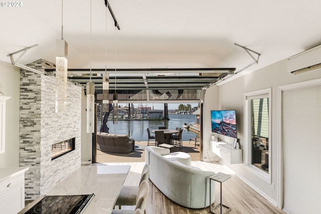 living room with a stone fireplace, light wood-type flooring, a wealth of natural light, and an AC wall unit