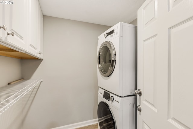 laundry room featuring cabinets and stacked washing maching and dryer