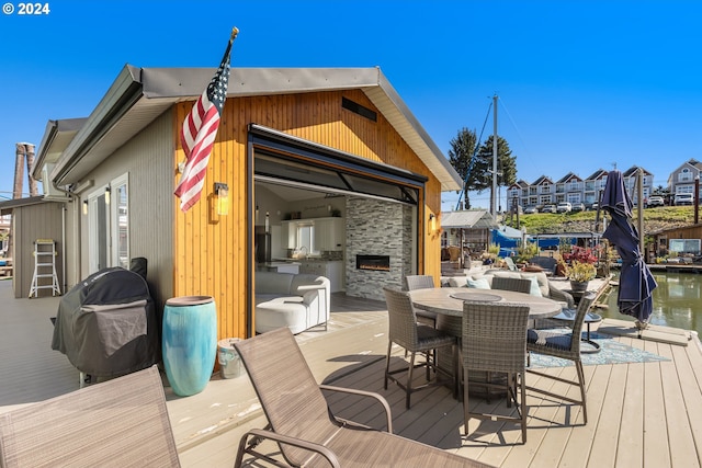 wooden terrace featuring a grill, a water view, and an outdoor stone fireplace