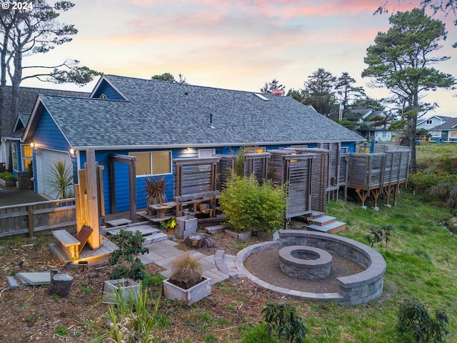 rear view of property with an outdoor fire pit, roof with shingles, a wooden deck, and a lawn