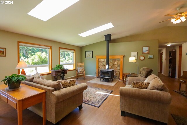 living room featuring light hardwood / wood-style floors, a wood stove, vaulted ceiling with skylight, and ceiling fan