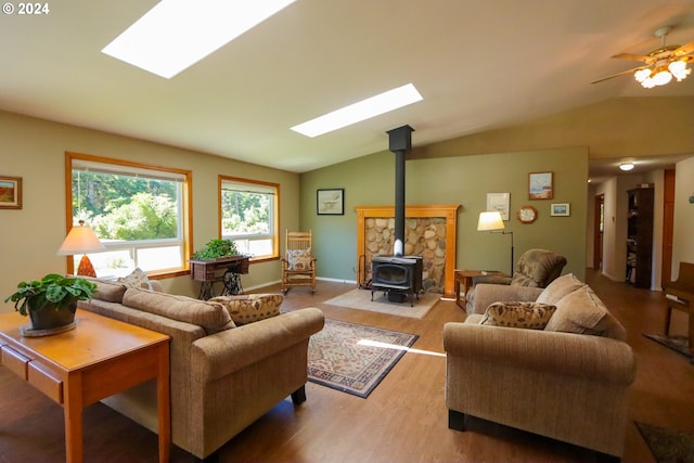 living room featuring wood-type flooring, lofted ceiling with skylight, ceiling fan, and a wood stove