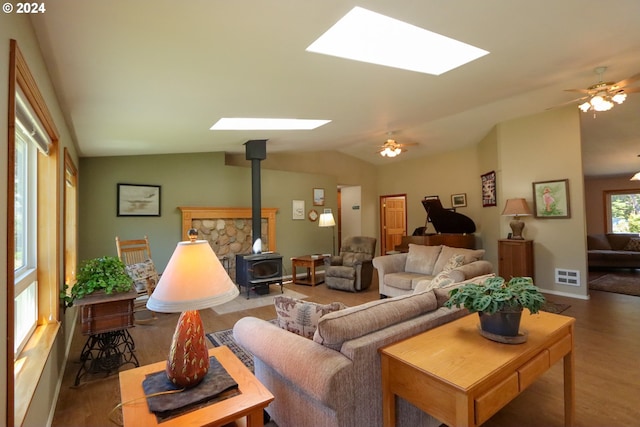 living room with dark wood-type flooring, lofted ceiling with skylight, ceiling fan, and a wood stove