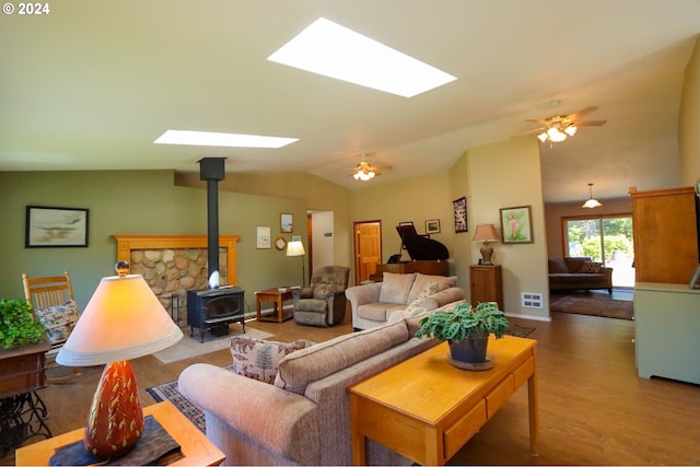 living room featuring hardwood / wood-style floors, ceiling fan, vaulted ceiling with skylight, and a wood stove