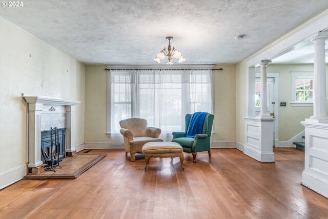 sitting room featuring hardwood / wood-style flooring, decorative columns, a tiled fireplace, and an inviting chandelier