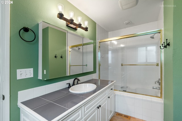 bathroom featuring wood-type flooring, vanity, and enclosed tub / shower combo