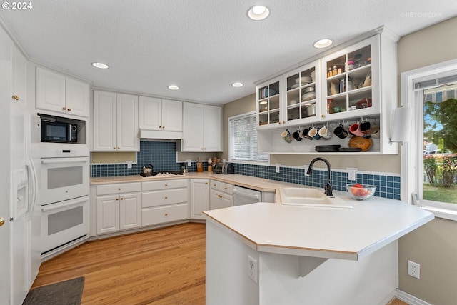 kitchen featuring sink, kitchen peninsula, light hardwood / wood-style floors, white appliances, and white cabinets