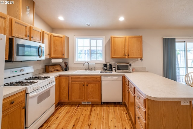 kitchen featuring white appliances, light countertops, a sink, and a peninsula