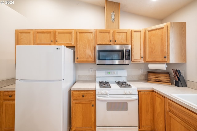 kitchen with white appliances, a sink, vaulted ceiling, light countertops, and light brown cabinetry