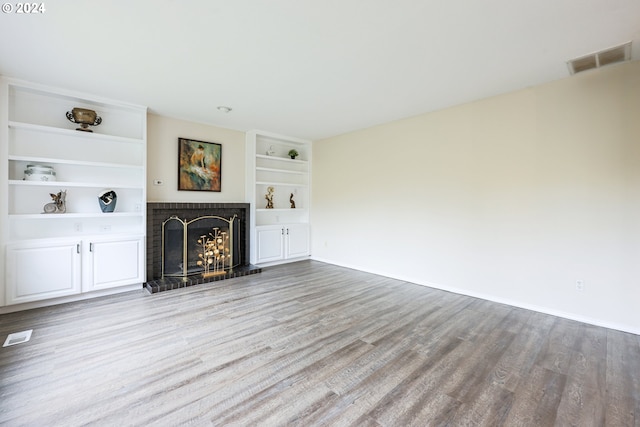 unfurnished living room with light hardwood / wood-style floors, a brick fireplace, and built in shelves