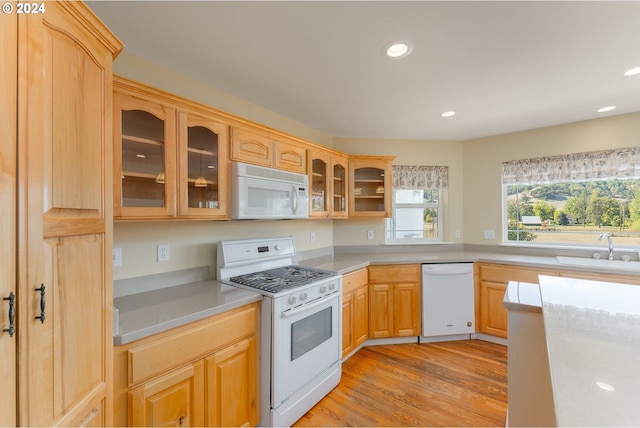 kitchen with light brown cabinets, light wood-type flooring, sink, and white appliances