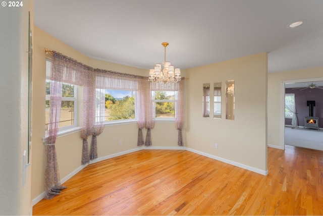 empty room with ceiling fan with notable chandelier, hardwood / wood-style floors, a wealth of natural light, and a wood stove