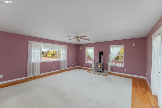 interior space with a wood stove, ceiling fan, light hardwood / wood-style flooring, and a healthy amount of sunlight