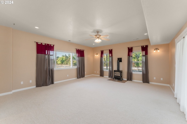 carpeted empty room featuring ceiling fan and a wood stove