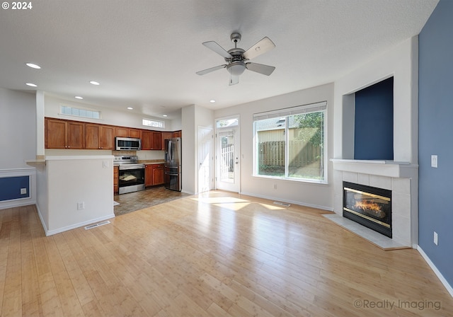 unfurnished living room featuring a fireplace, a textured ceiling, ceiling fan, and light hardwood / wood-style floors