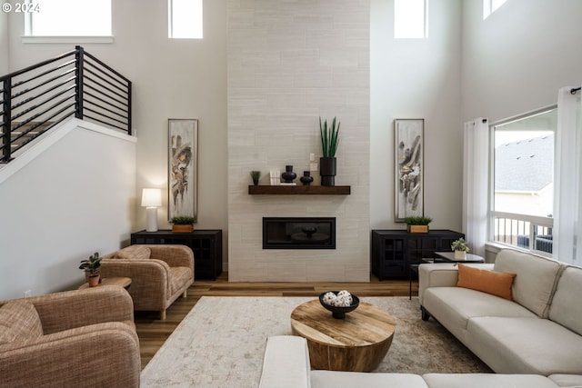 living room with a healthy amount of sunlight, a towering ceiling, wood finished floors, and a tiled fireplace