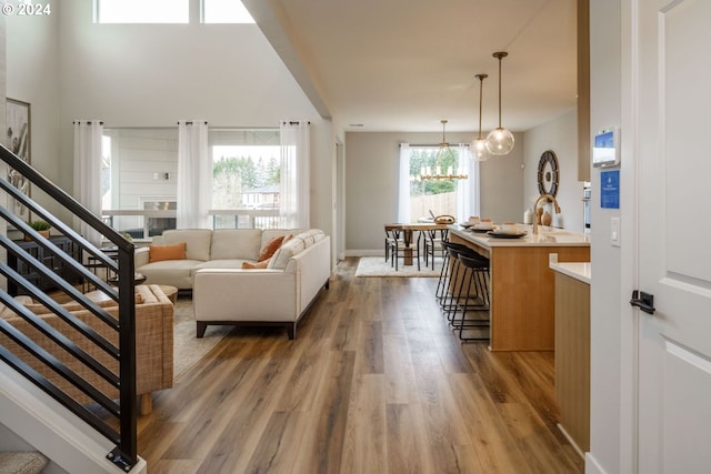 living room featuring a notable chandelier, stairway, baseboards, and wood finished floors