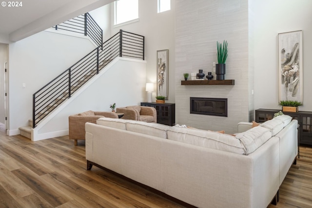 living area featuring a fireplace, wood finished floors, a towering ceiling, baseboards, and stairs