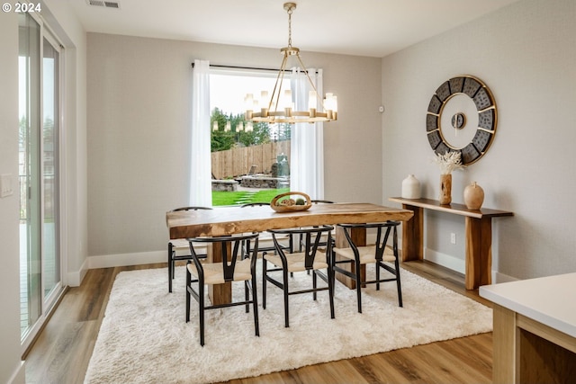 dining space featuring baseboards, light wood-type flooring, visible vents, and an inviting chandelier