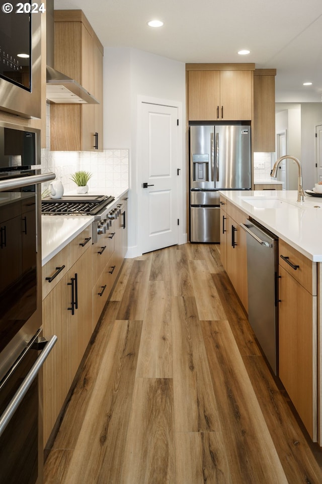 kitchen with tasteful backsplash, stainless steel appliances, light countertops, light wood-type flooring, and a sink