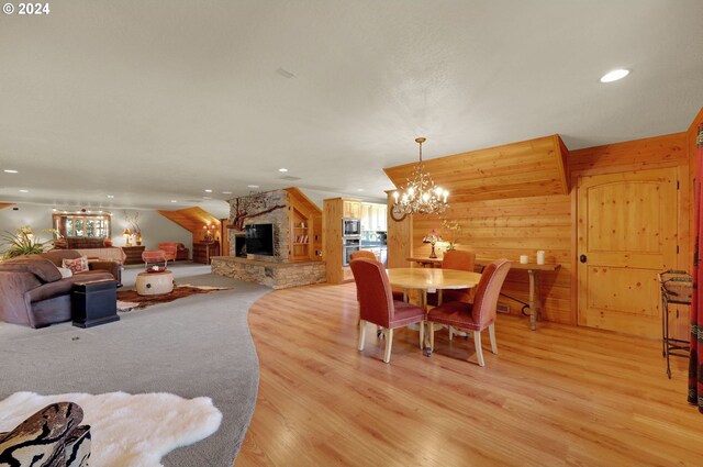 dining area with a chandelier, light wood-type flooring, and a stone fireplace