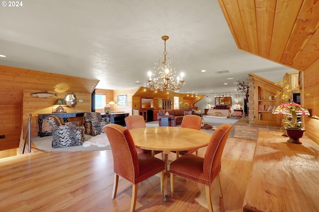 dining room featuring light wood-type flooring, wooden walls, and an inviting chandelier