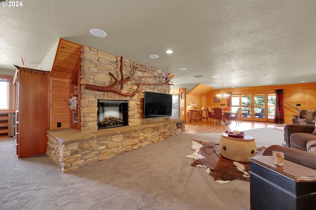 carpeted living room with wooden walls, a fireplace, a textured ceiling, and a notable chandelier