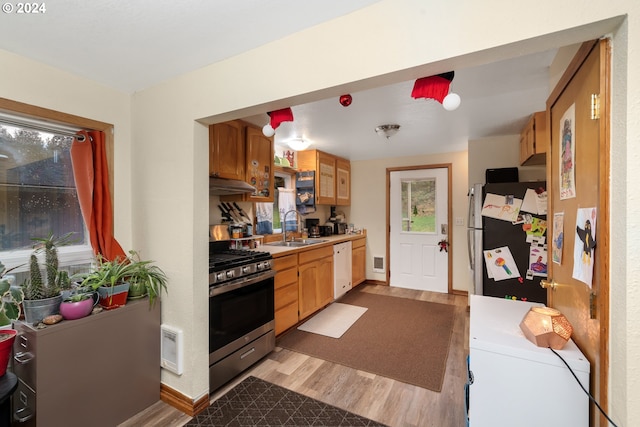 kitchen featuring light wood-style flooring, under cabinet range hood, a sink, light countertops, and appliances with stainless steel finishes