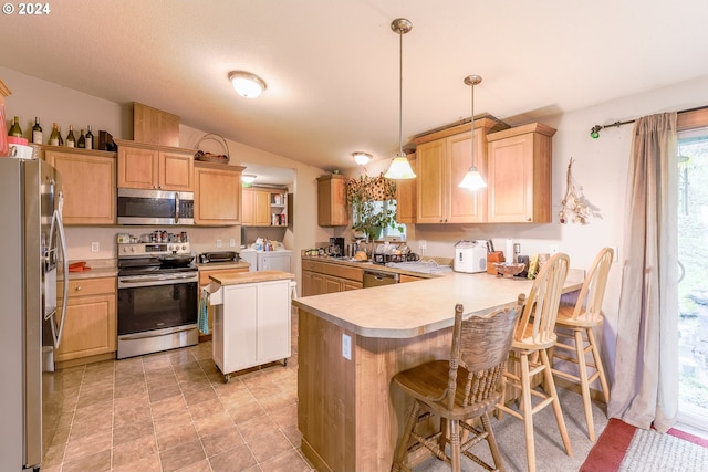 kitchen with appliances with stainless steel finishes, a breakfast bar, light tile floors, decorative light fixtures, and washing machine and dryer