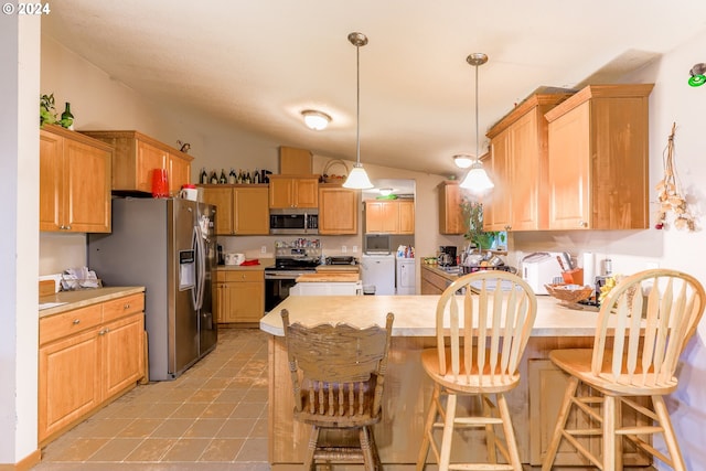 kitchen with washing machine and clothes dryer, a breakfast bar, stainless steel appliances, vaulted ceiling, and decorative light fixtures