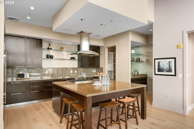 kitchen featuring a kitchen bar, light stone countertops, island exhaust hood, stainless steel gas cooktop, and sink