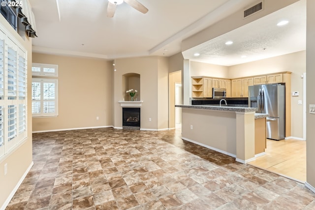 kitchen featuring appliances with stainless steel finishes, ceiling fan, sink, light brown cabinets, and dark stone countertops