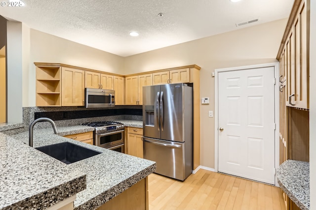 kitchen with sink, stainless steel appliances, a textured ceiling, light brown cabinetry, and light wood-type flooring