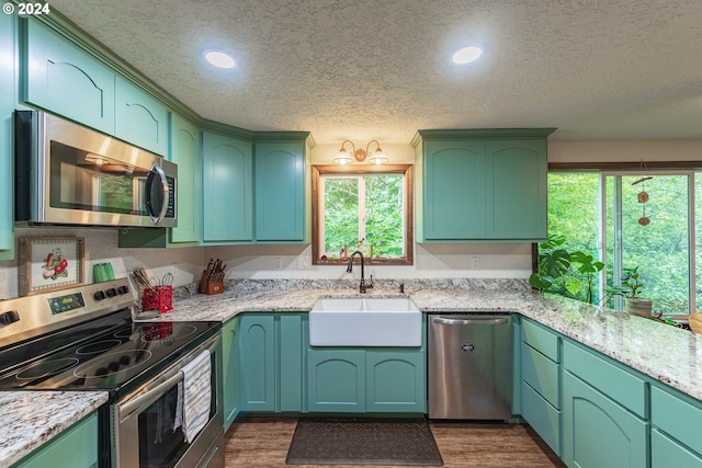 kitchen with appliances with stainless steel finishes, dark wood finished floors, a sink, and a textured ceiling