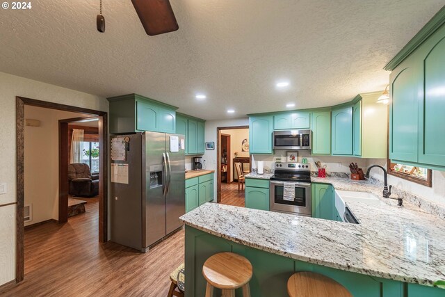 kitchen featuring hardwood / wood-style flooring, sink, light stone counters, appliances with stainless steel finishes, and kitchen peninsula