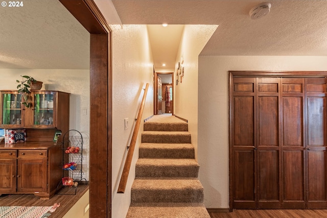 staircase with a textured ceiling, wood finished floors, and a textured wall