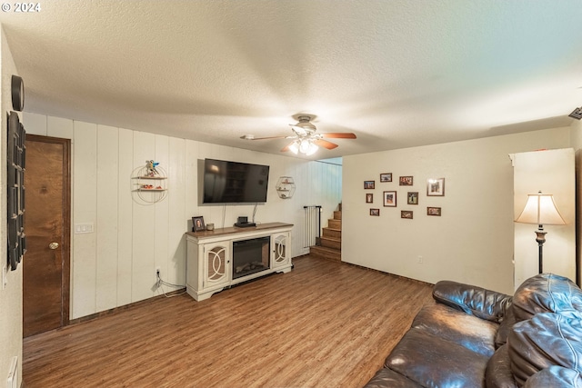 living area with a ceiling fan, wood finished floors, a textured ceiling, and stairs