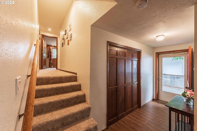 stairway featuring a textured ceiling, baseboards, wood finished floors, and a textured wall