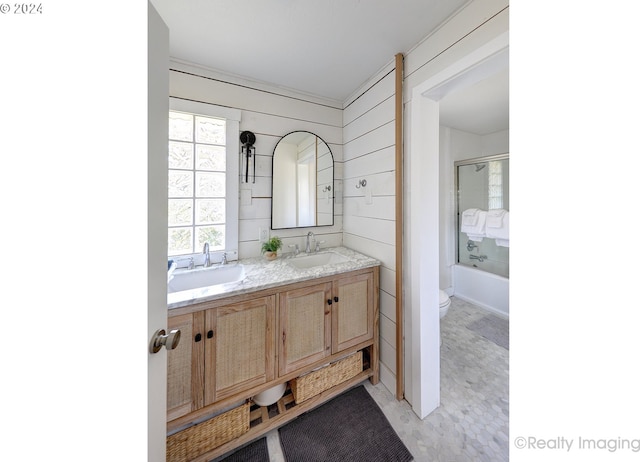 full bathroom with wood walls, shower / bath combination with glass door, vanity, and toilet